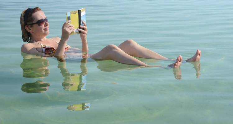 Persona flotando mientras lee un libro en un cuerpo de agua cristalina.