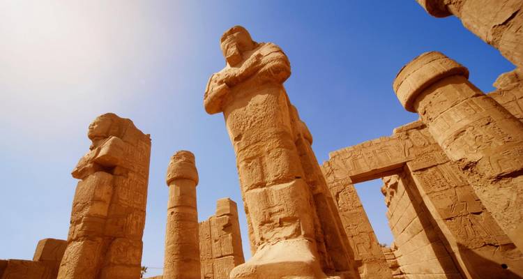 Estatuas y pilares del antiguo Egipto bajo un cielo azul brillante.