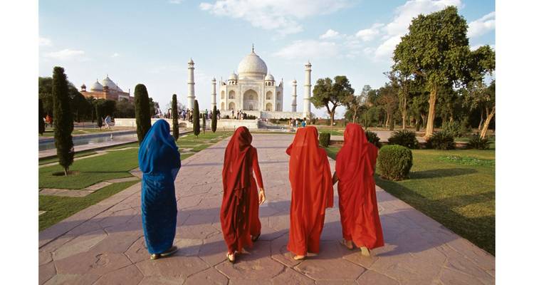 Frauen in lebendigen Saris, die auf einem Steinweg unter blauem Himmel zum Taj Mahal gehen.
