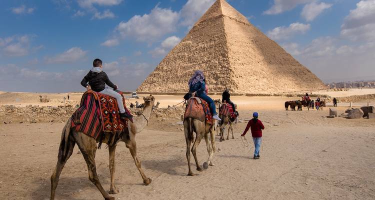 Cavaliers de chameaux s'approchant d'une pyramide sous un ciel dégagé.