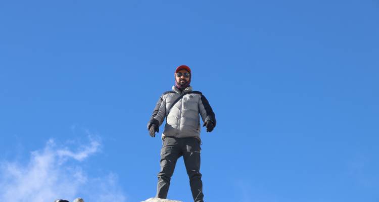 A man standing on a rocky peak wearing a winter jacket.