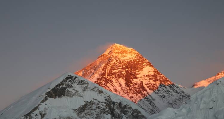 Snow-covered mountain peak glowing orange during sunset.