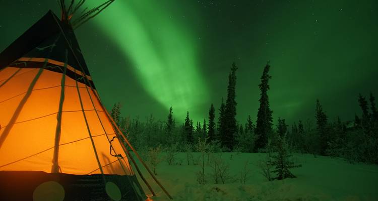Auroras boreales sobre un tipi iluminado en un paisaje de bosque nevado.