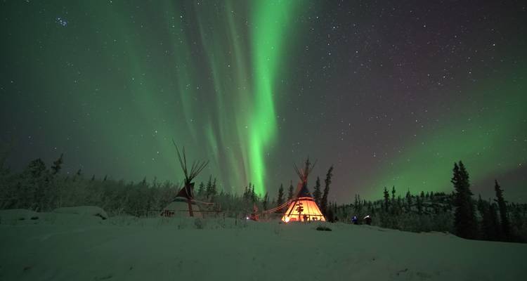 Auroras boreales con cielos estrellados sobre tipis en un paisaje nevado.