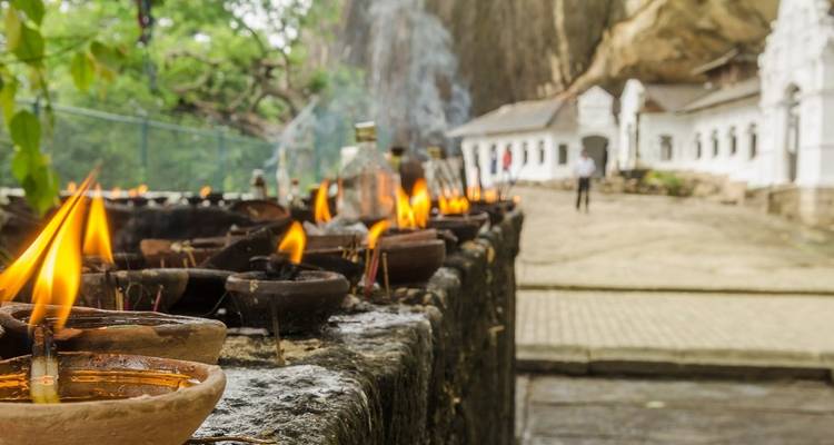 Lámparas de aceite encendidas sobre una superficie de piedra con un templo al fondo.