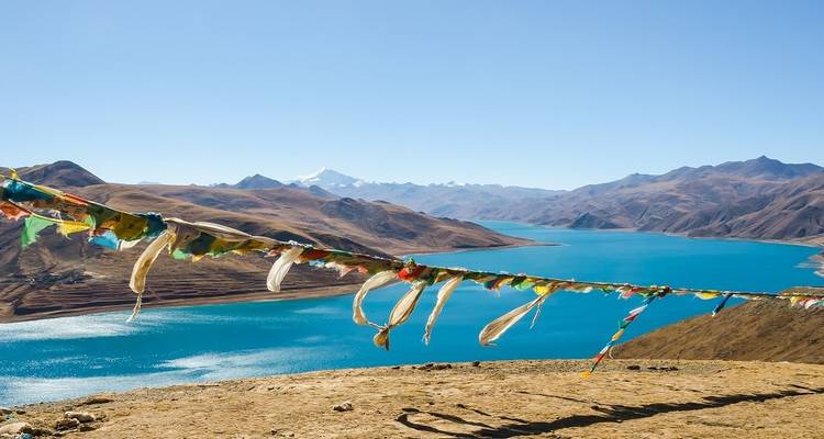Prayer flags fluttering above the brilliant turquoise waters of Yamdrok Lake amid brown Tibetan mountains