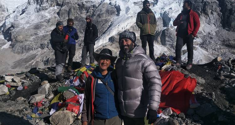 Wandelaars die poseren op rotsachtig terrein met besneeuwde bergen op de achtergrond.