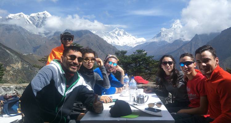 Groep mensen verzameld aan een tafel met bergen op de achtergrond.