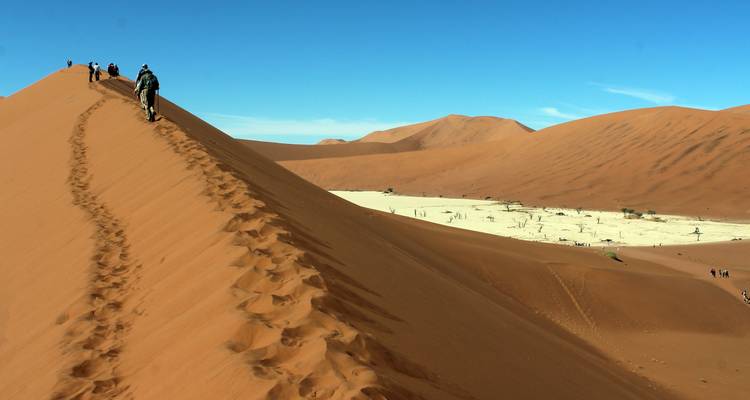 Group hiking up a large sand dune with a desert crater.