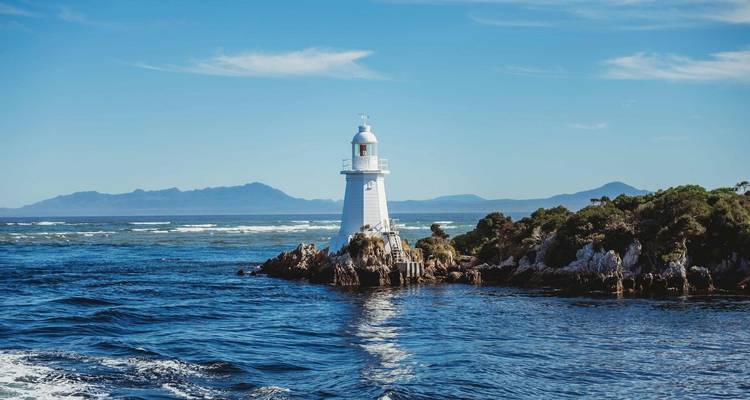 Phare blanc perché sur un îlot rocheux entouré d'une mer bleu profond avec des chaînes de montagnes lointaines.