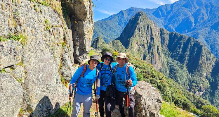 Trois randonneurs posent sur un sentier avec le Machu Picchu et les montagnes en arrière-plan.