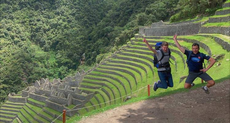 Dos excursionistas están saltando en el aire contra ruinas en terrazas.