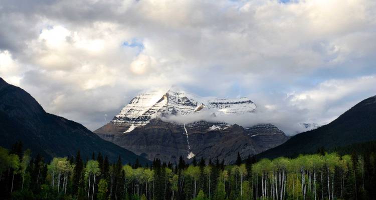 El Monte Robson cubierto de nieve se eleva sobre bosques oscuros bajo un cielo nublado y dramático.