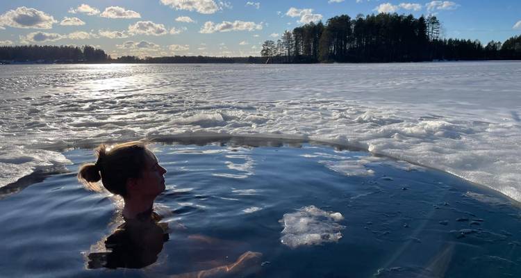 Una mujer disfruta nadando en agua helada en un agujero circular tallado en un lago congelado bajo cielos despejados.