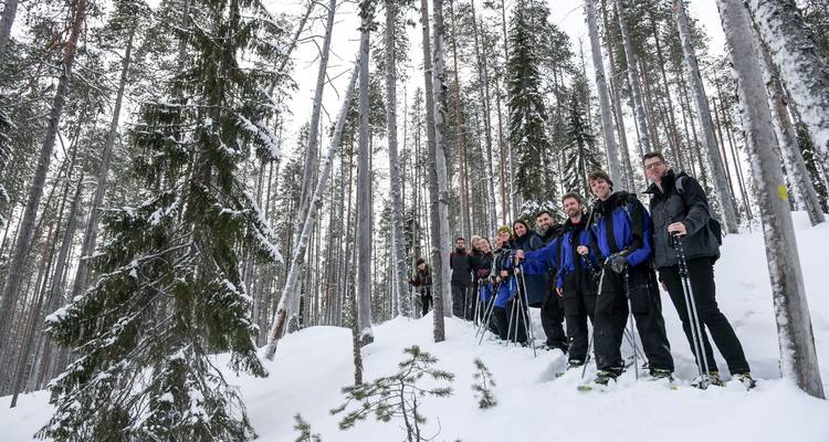 Gran grupo de personas haciendo raquetas de nieve en un bosque nevado.
