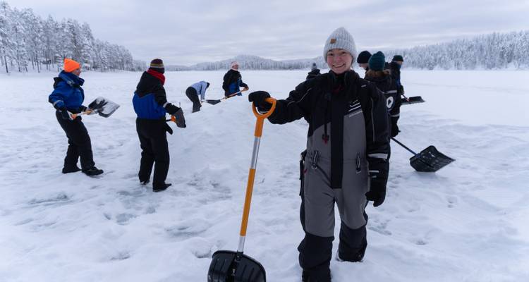 Los viajeros cavan y moldean un gran montón de nieve en un lago congelado, preparando un iglú en el paisaje ártico.