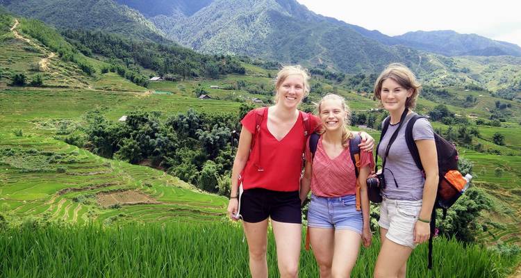 Trois personnes posant sur une colline avec des champs en terrasses et des montagnes en arrière-plan.