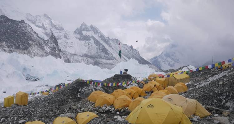 Expeditietenten gegroepeerd op rotsachtige morene op Everest Basiskamp met ijsval daarachter