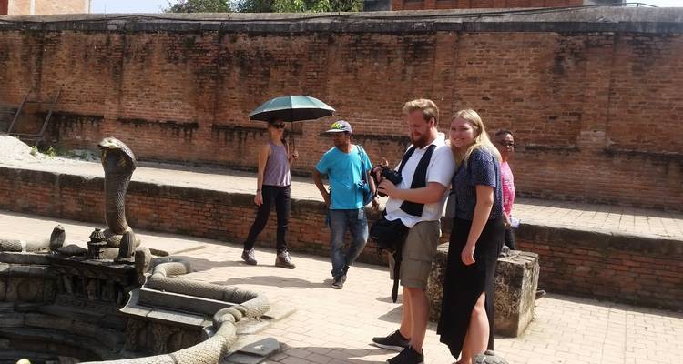 Tourists observing an ancient stone serpent fountain in a sunken courtyard