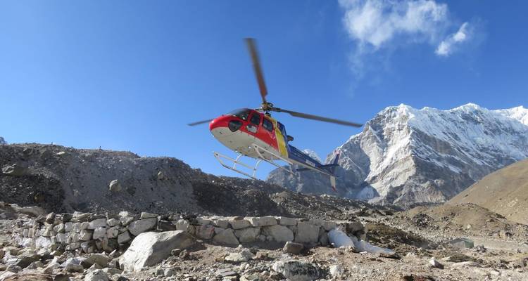 A colorful rescue helicopter hovering above rocky terrain with dramatic snowy peaks behind