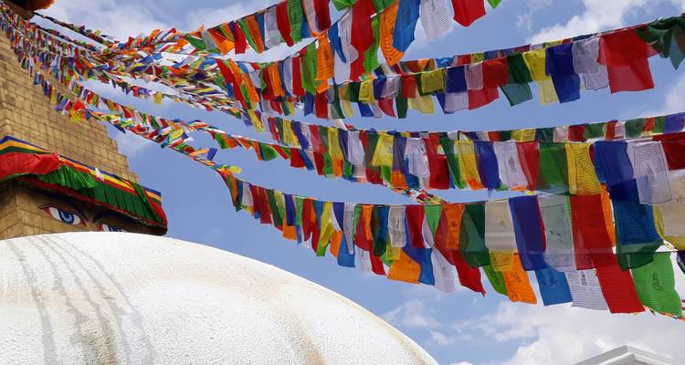 Prayer flags fluttering around a stupa with a blue sky.