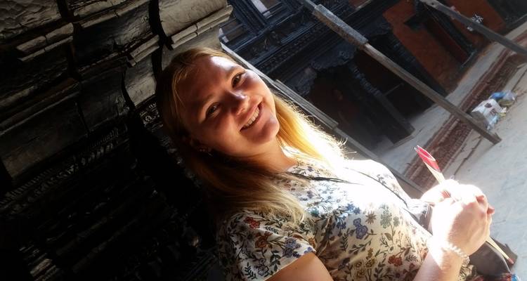 A smiling person standing near intricate temple carvings.