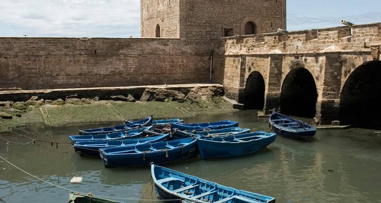 Rangée de bateaux de pêche en bois bleu emblématiques amarrés à côté d'une forteresse en pierre dans le port d'Essaouira.