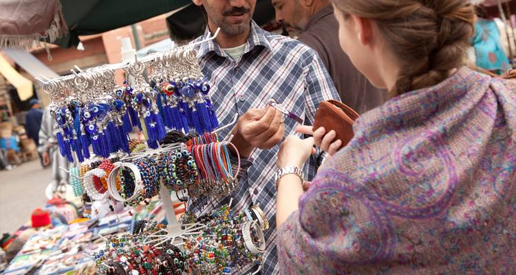 Une vendeuse de marché présentant des bijoux colorés à une cliente dans un étal extérieur.