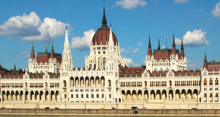 El ornamentado Edificio del Parlamento Húngaro se alza majestuosamente a orillas del Danubio bajo un cielo azul.