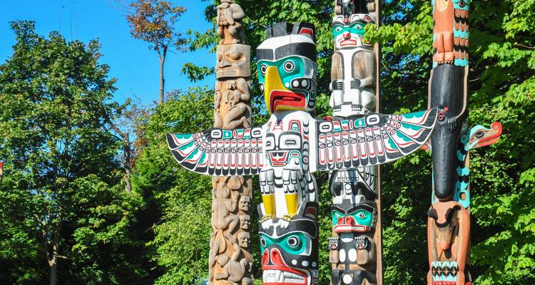 Colorful First Nations totem poles standing tall among lush green trees under a clear blue sky.