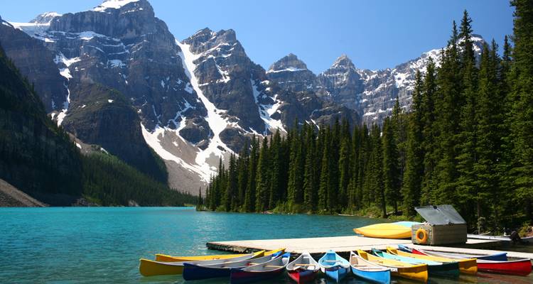 Vibrant canoes lined up on the dock of stunning turquoise Moraine Lake beneath dramatic snow-capped peaks.