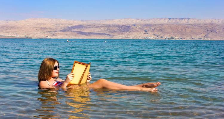 Personne flottant et lisant dans la mer Morte avec des montagnes désolées au loin.