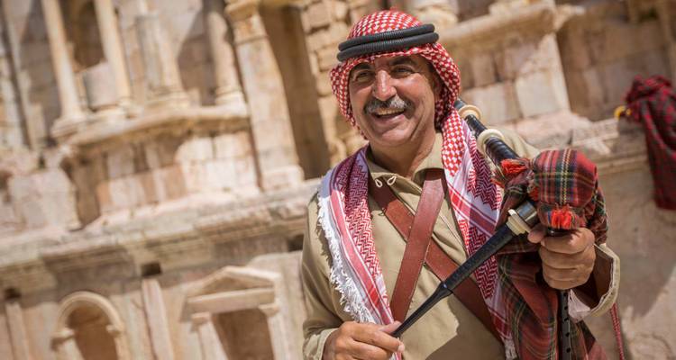 Un homme en tenue traditionnelle sur un site historique, souriant et posant avec une épée.