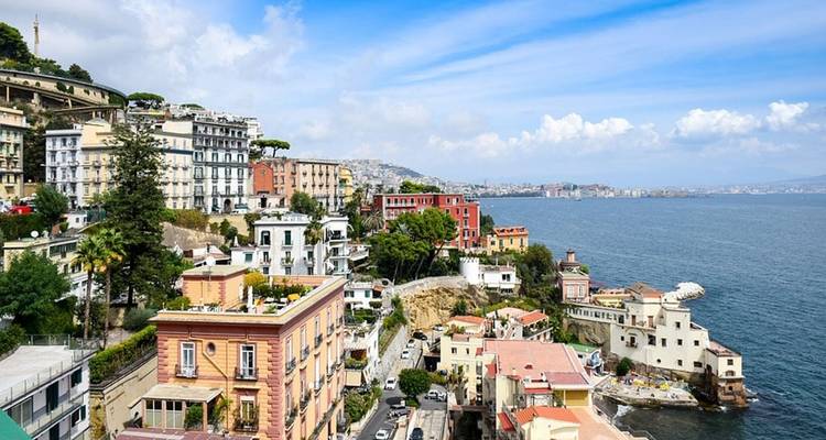 Bright coastal panorama of colorful buildings stacked on a hillside overlooking a deep-blue bay on a sunny day.