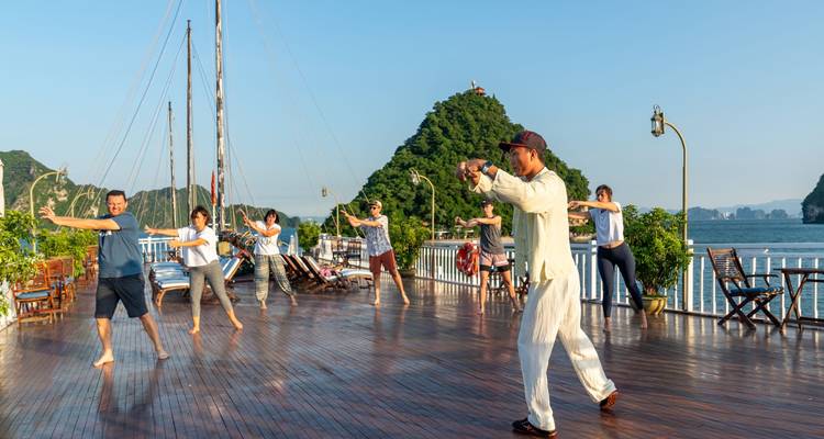Mensen die Tai Chi beoefenen op een terras met kalkstenen karstformaties op de achtergrond.