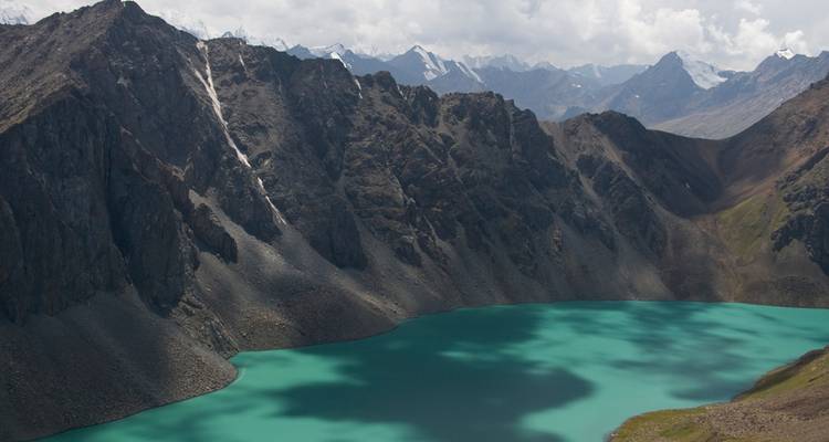 Lago alpino turquesa anidado bajo picos escarpados cubiertos de nieve en las montañas de Kirguistán.