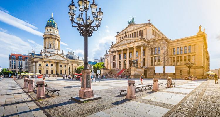 Vue ensoleillée sur la place Gendarmenmarkt de Berlin avec la Cathédrale française, le Konzerthaus et des visiteurs épars traversant la place.