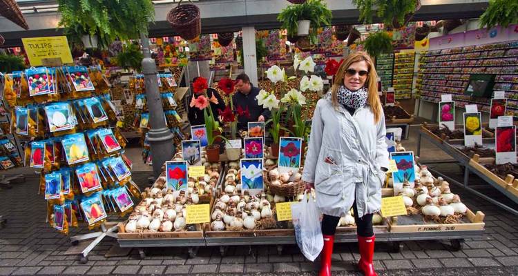 Indoor flower market stall in Amsterdam with colourful tulip bulbs and a smiling shopper in red boots.