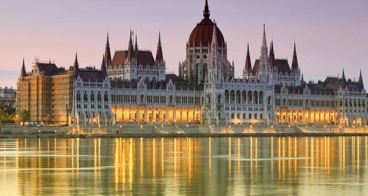 Illuminated Hungarian Parliament building reflected in the Danube River at dusk in Budapest.