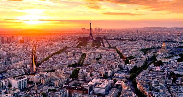 Sunset aerial of Paris with the Eiffel Tower standing above the sprawling city bathed in orange light.