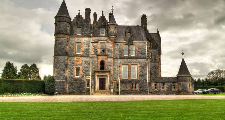 Stenen kasteel Belfast met torentjes en gemanicuurde gazon onder dreigende wolken.