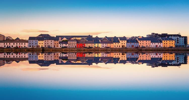 Kleurrijke huizen aan de havenkant in Galway perfect weerspiegeld in stil water bij schemering.