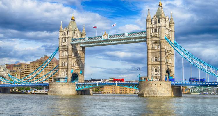 Iconic blue-accented Tower Bridge spanning the River Thames beneath dramatic clouds.