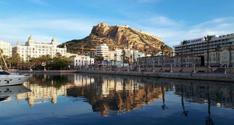 Yacht in Alicante harbour with castle-topped mountain mirrored in the water