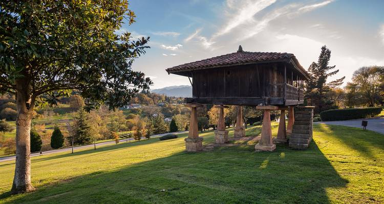 Traditionelle, erhöhte Holzgetreidespeicher auf Steinpfeilern in einer üppigen ländlichen asturischen Landschaft am späten Nachmittag.
