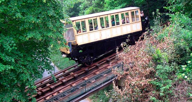 Vintage holzverkleidete Standseilbahn fährt durch belaubten Wald auf Gleisen in der Nähe von Braga.