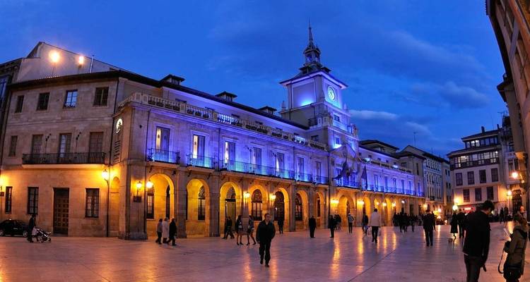 Blau beleuchtetes Rathaus von Oviedo und Platz voller Abendspaziergeher