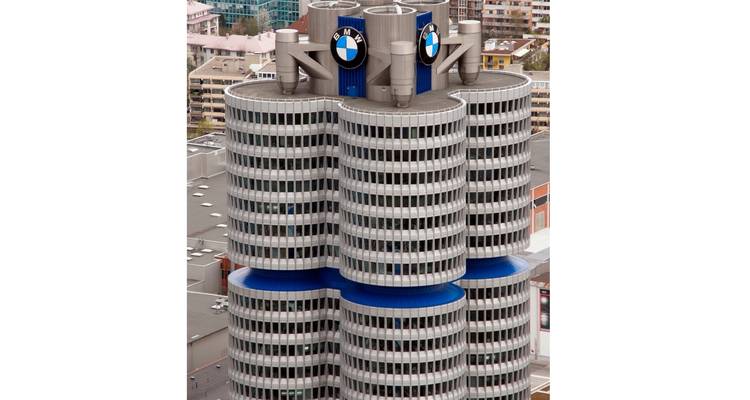 Vista aérea de primer plano de la torre sede de cuatro cilindros de BMW con logotipos azules contra un telón de fondo urbano.