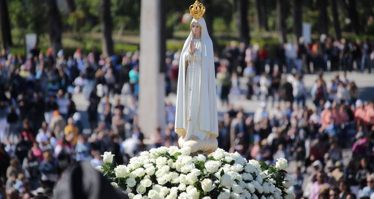 Estatua procesional de Nuestra Señora de Fátima rodeada de rosas blancas y una gran multitud de peregrinos
