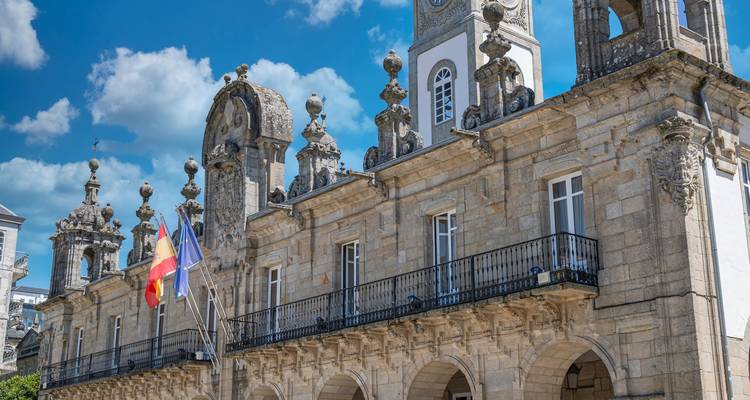 Detalle de edificio histórico de piedra con balaustradas ornamentadas y torre del reloj en Lugo, España.